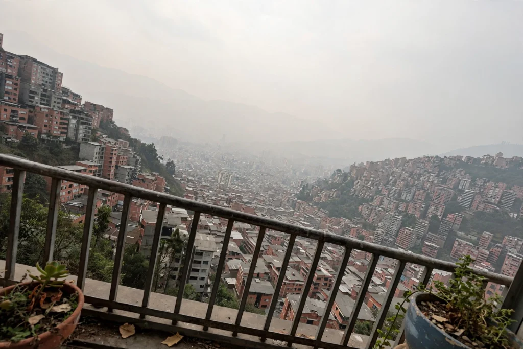 View from a balcony railing over a mountain valley filled with red-brick apartment towers, with distant ridgelines fading into pale haze